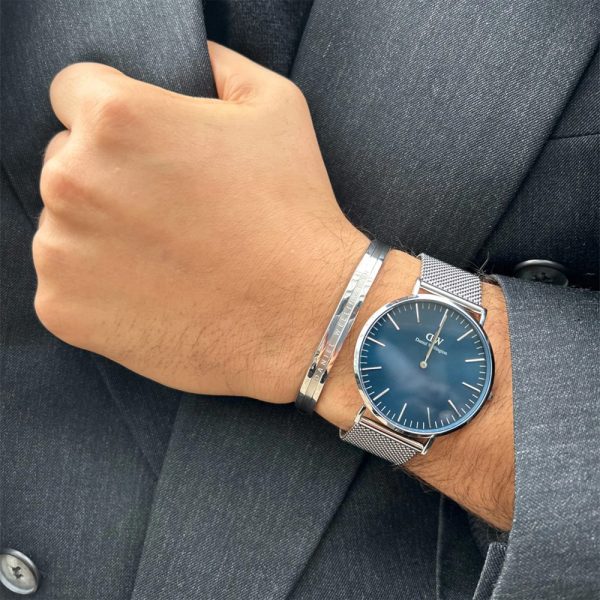 שעון יד Daniel Wellington רצועת רשת כסופה לגבר רקע כחול דגם DW00100628 בתקריב על יד